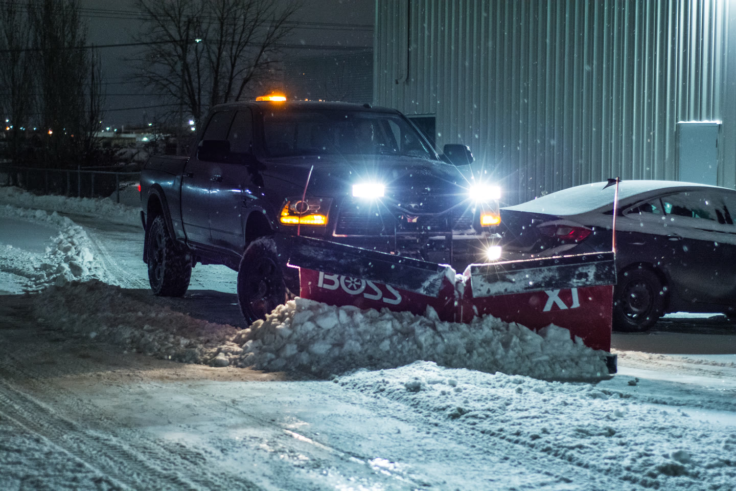 A Formela Bros truck plowing snow beside a commercial building